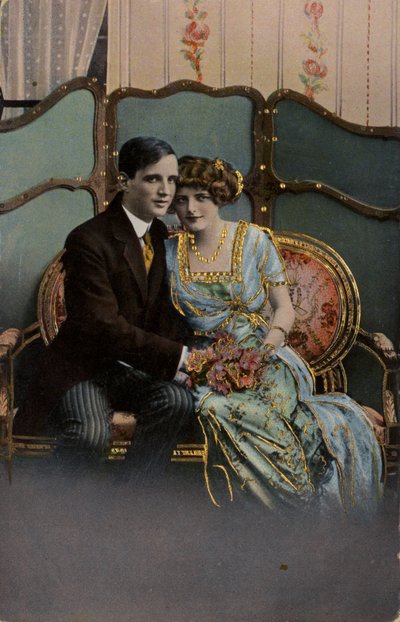 Couple holding a bouquet of flowers, seated on a loveseat by English Photographer